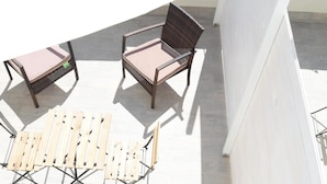 A patio with three wooden chairs and a table, a round table lamp, and a white wall.