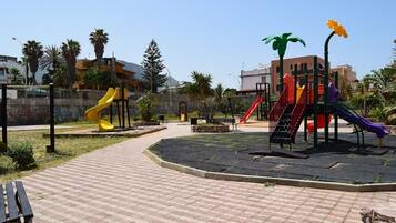 Explore a playground with slides and climbing elements, surrounded by a paved walkway and lush greenery.