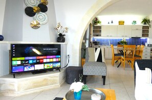 A living room with a flat-screen TV, a dining area with a table and chairs, and a kitchen with cabinets and a blue-tiled backsplash. - Luxury Villa in Gavalochori with Heated Pool & Panoramic Views (Gavalochori)