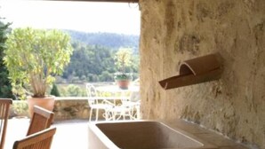 A rustic outdoor seating area with a stone sink, wooden chairs, and a view of a forested landscape. - Village house with heated pool in the Luberon for 14 people (Ansouis)