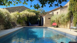 A rectangular swimming pool with clear blue water, surrounded by stone walls and vegetation. - Village house with heated pool in the Luberon for 14 people (Ansouis)