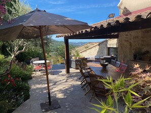 Une terrasse extérieure avec une table et des chaises, un grand parasol et une vue sur le paysage environnant.