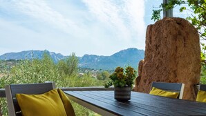 A wooden table with a potted plant, two chairs with yellow cushions, and a large rock in the background. - La Casa di Alice Turchese (Olbia)