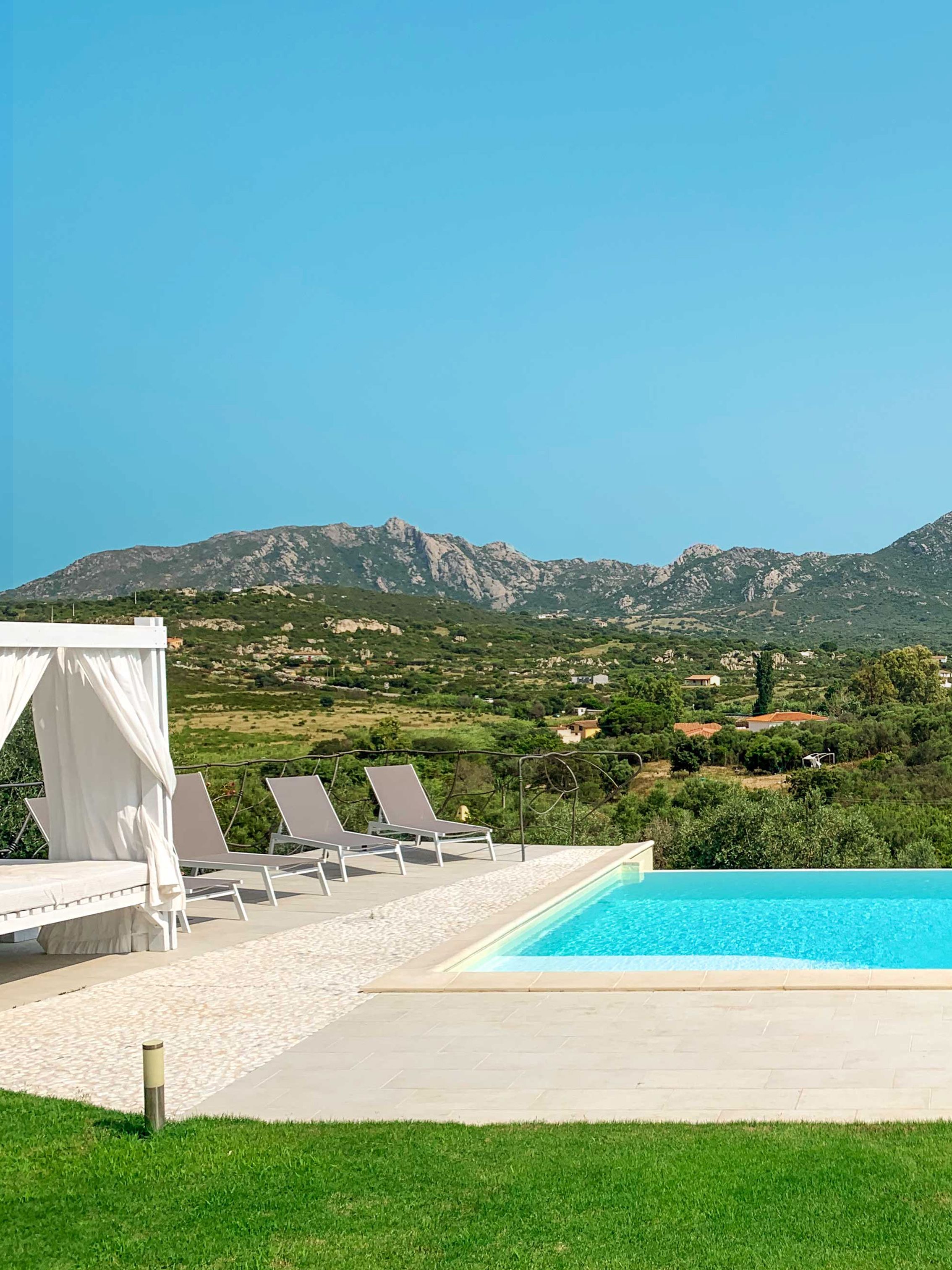 A poolside area with lounge chairs and a canopy, overlooking a mountainous landscape.