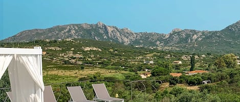 A poolside area with lounge chairs and a canopy, overlooking a mountainous landscape.