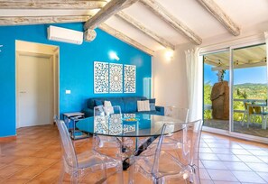 Een kamer met een blauwe wand, een glazen tafel met stoelen, een bank en uitzicht door een glazen deur.