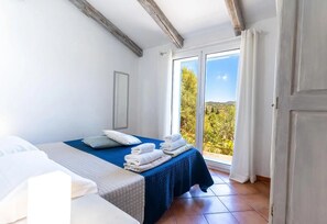 A bedroom with a bed, a window with a view of greenery, and a door.