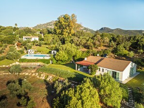 A large estate with a swimming pool, multiple buildings, and a mountainous backdrop.