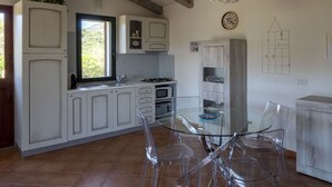 A kitchen with white cabinets, a glass table, and clear chairs. - La Casa di Alice Turchese (Olbia)