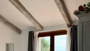 A bedroom with a bed, a window with curtains, a view of greenery, and a wooden ceiling. - La Casa di Alice Turchese (Olbia)