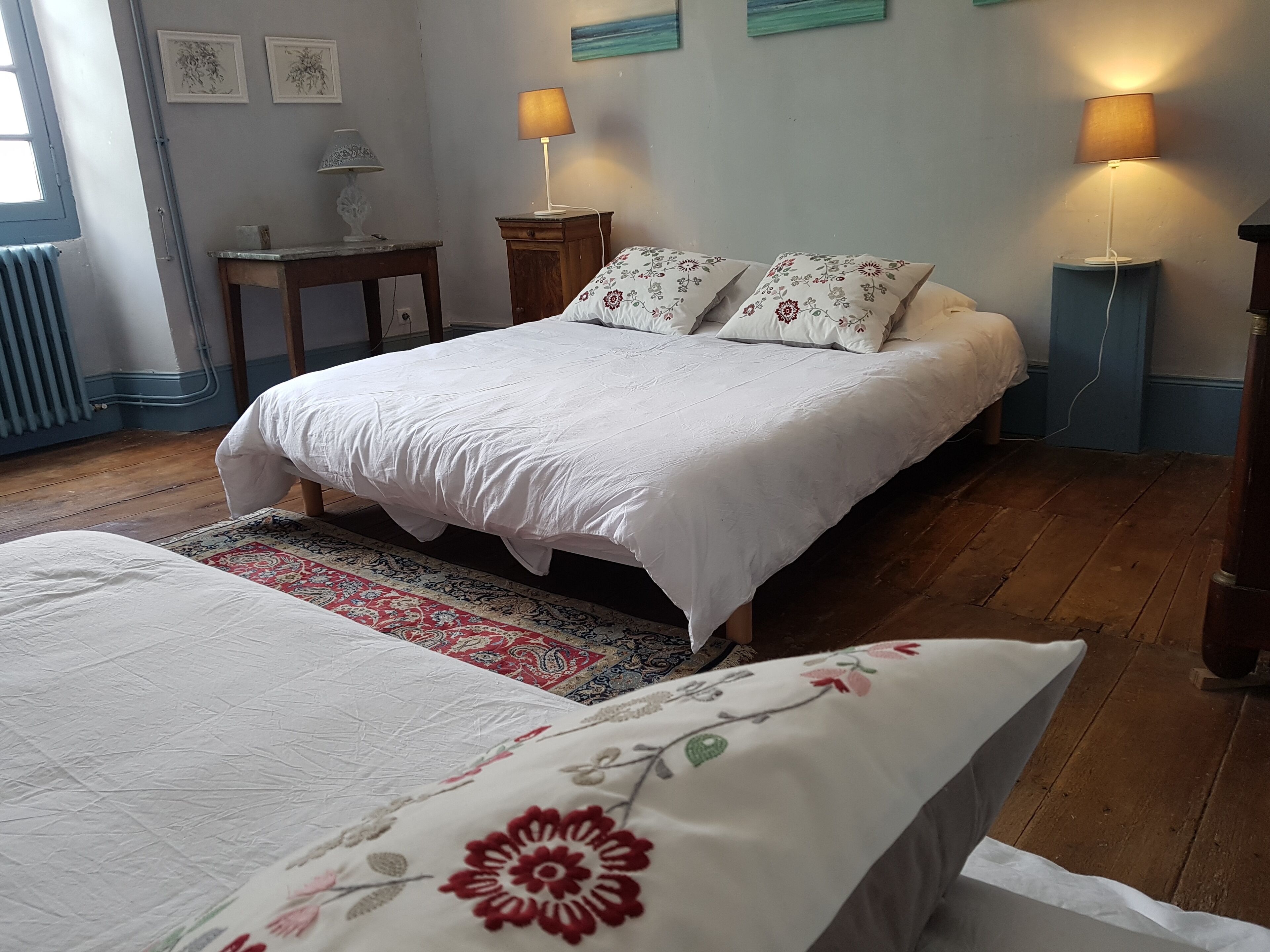 Une chambre à coucher avec un grand lit, deux tables de chevet, une commode, un radiateur et une fenêtre.