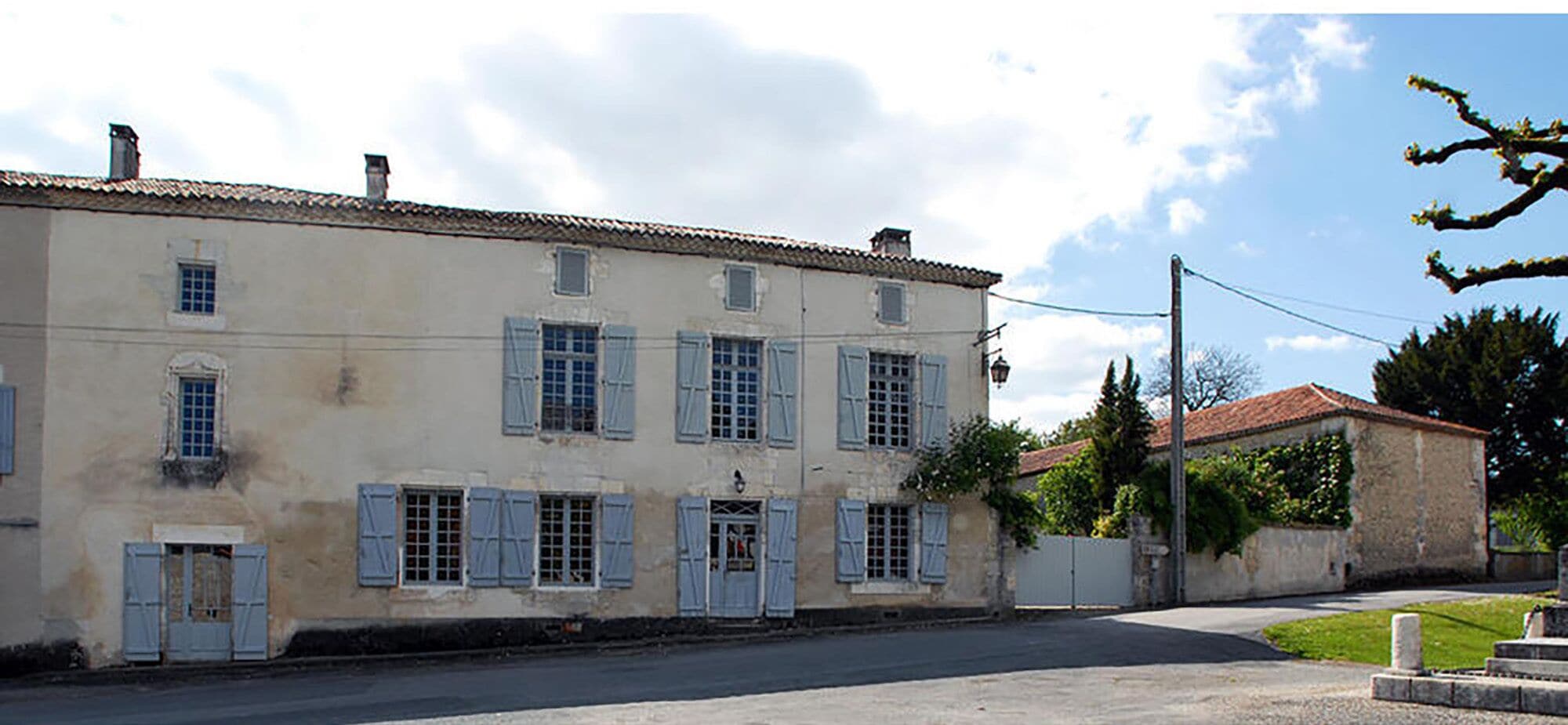 A two-story building with a tiled roof, multiple windows with shutters, and a paved street in front.