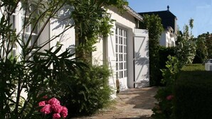 A white building with a large garage door, surrounded by lush greenery and a stone pathway. - CHARMING HOUSE (Le Pouliguen)
