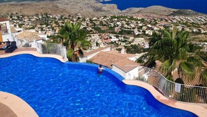 Une piscine offrant une vue sur une ville côtière et sur des montagnes en arrière-plan.