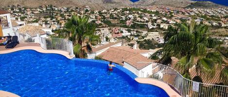 A swimming pool with a view of a coastal town and mountains in the background.
