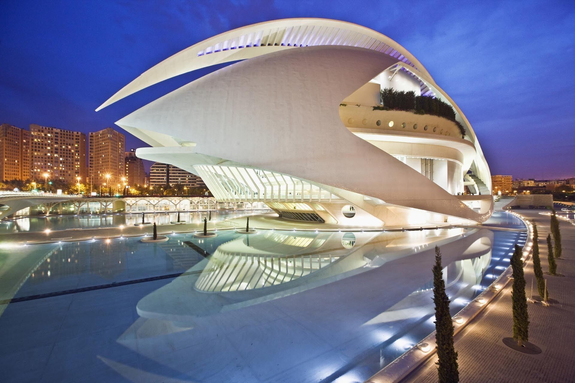 A modern architectural building with a unique curved design, surrounded by a reflective pool and a bridge.
