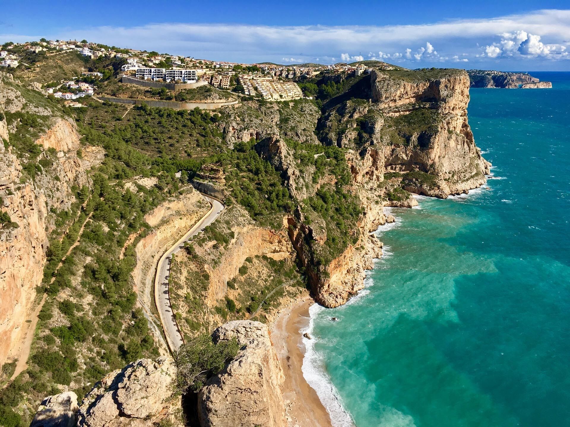 A coastal landscape with a winding road, cliffs, and a beach.