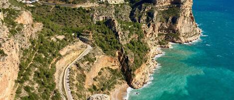 A coastal landscape with a winding road, cliffs, and a beach.