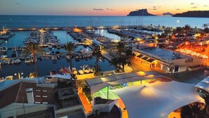 Un port de plaisance au crépuscule, avec des bateaux amarrés, un espace de repos abrité et des bâtiments dotés de balcons.