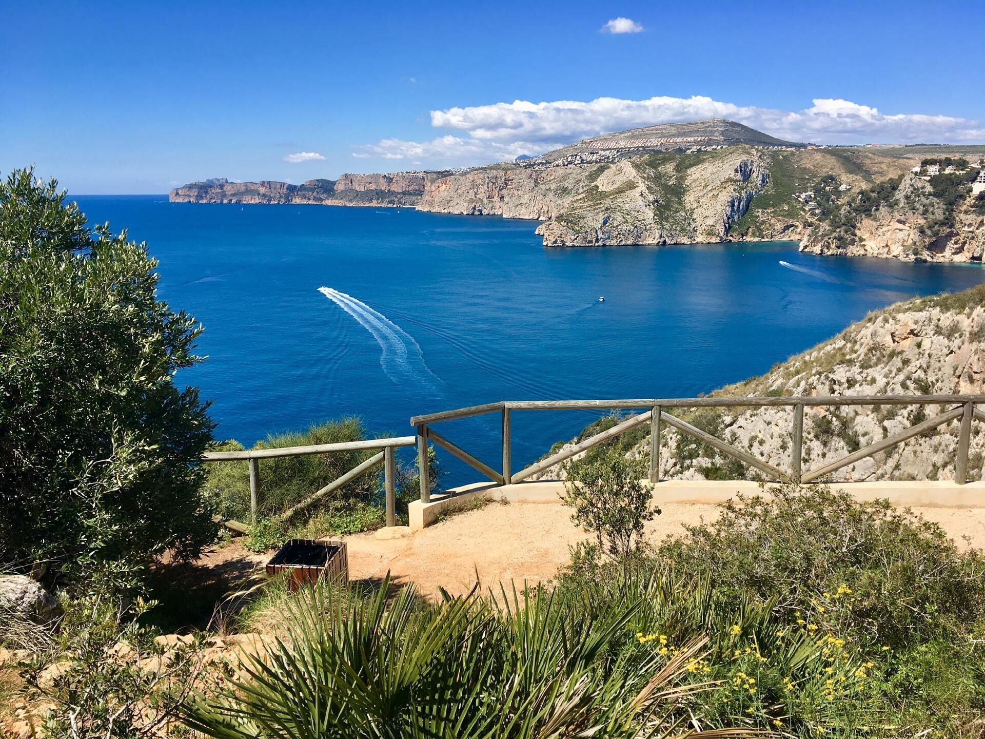 A coastal view with a wooden walkway leading to a cliff overlooking the sea.