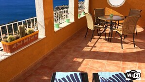 Une terrasse avec une table et des chaises, une vue sur la mer et des plantes en pot.