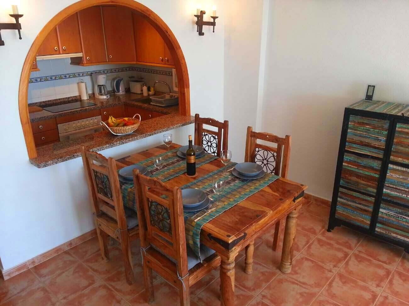 Un coin repas avec une table et des chaises en bois, une cuisine avec des meubles de rangement en bois et un sol carrelé.