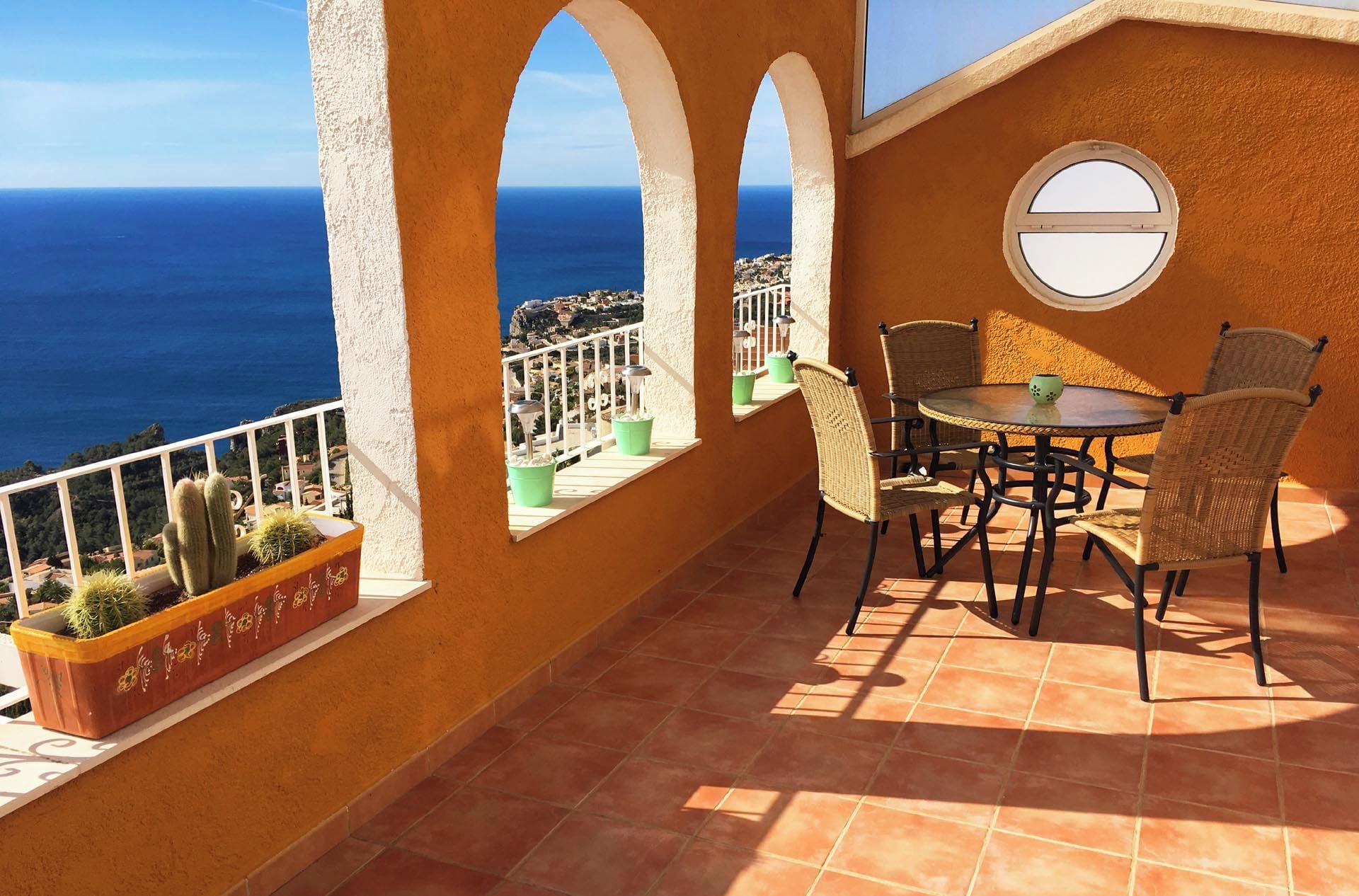 Eine Terrasse mit Tisch und Stühlen, Blick auf das Meer und Kübelpflanzen.