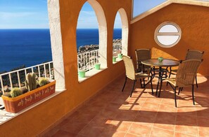 A terrace with a table and chairs, a view of the sea, and potted plants.