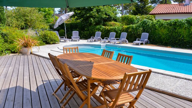 Eine Holzdielenfläche mit Billardtisch und Stühlen, umgeben von Liegestühlen und einem Pool.