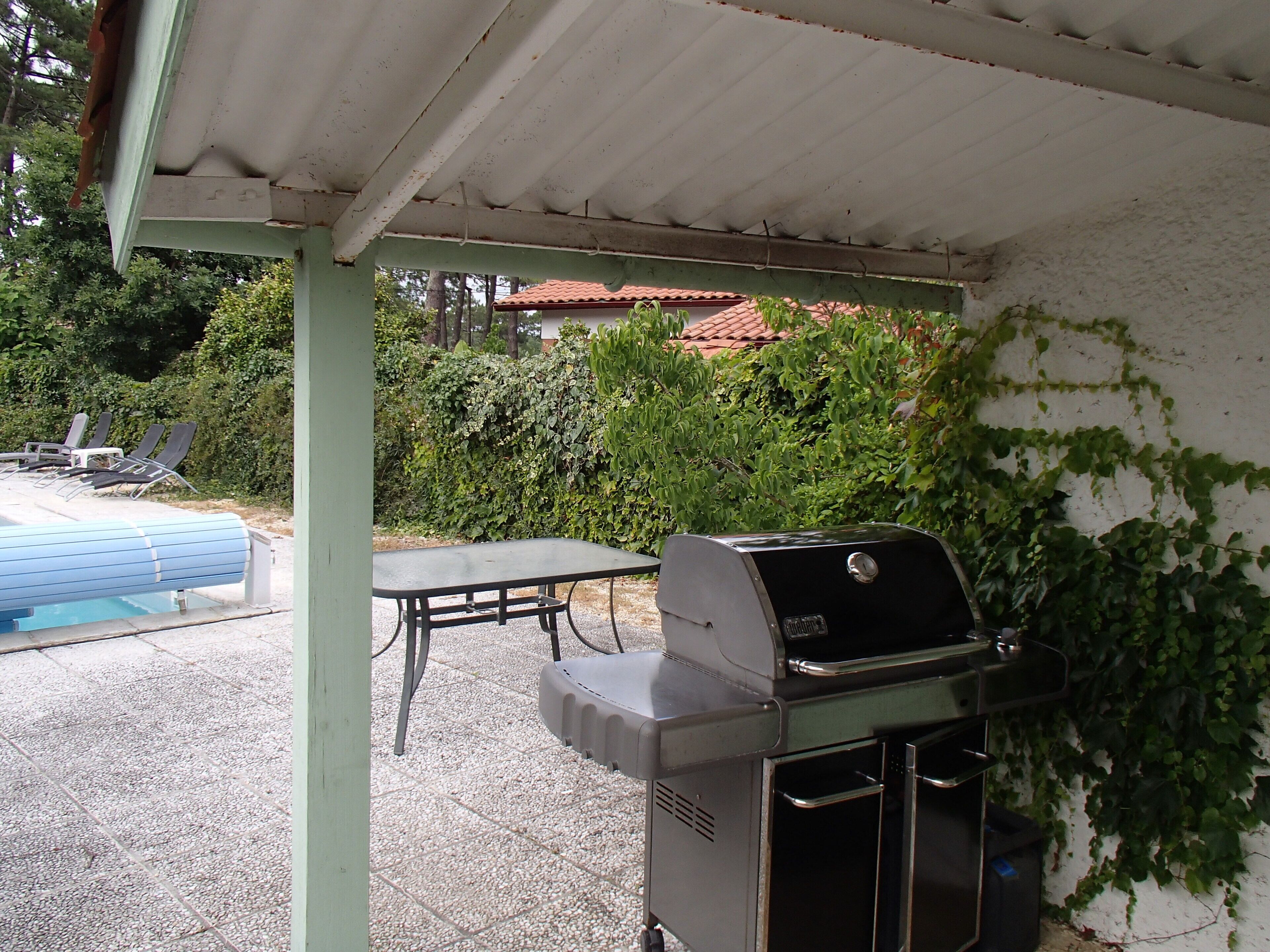 Un patio techado con una parrilla, piscina y una mesa con sillas.