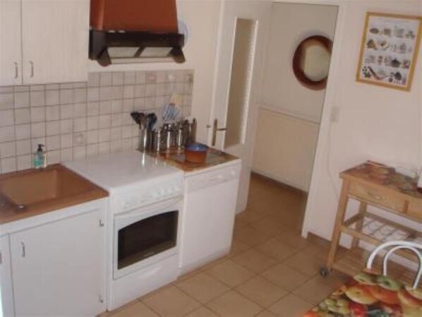 Una cocina compacta con armarios blancos, lavavajillas y horno pequeño. Hay una encimera de madera con diversos utensilios de cocina y un fregadero.