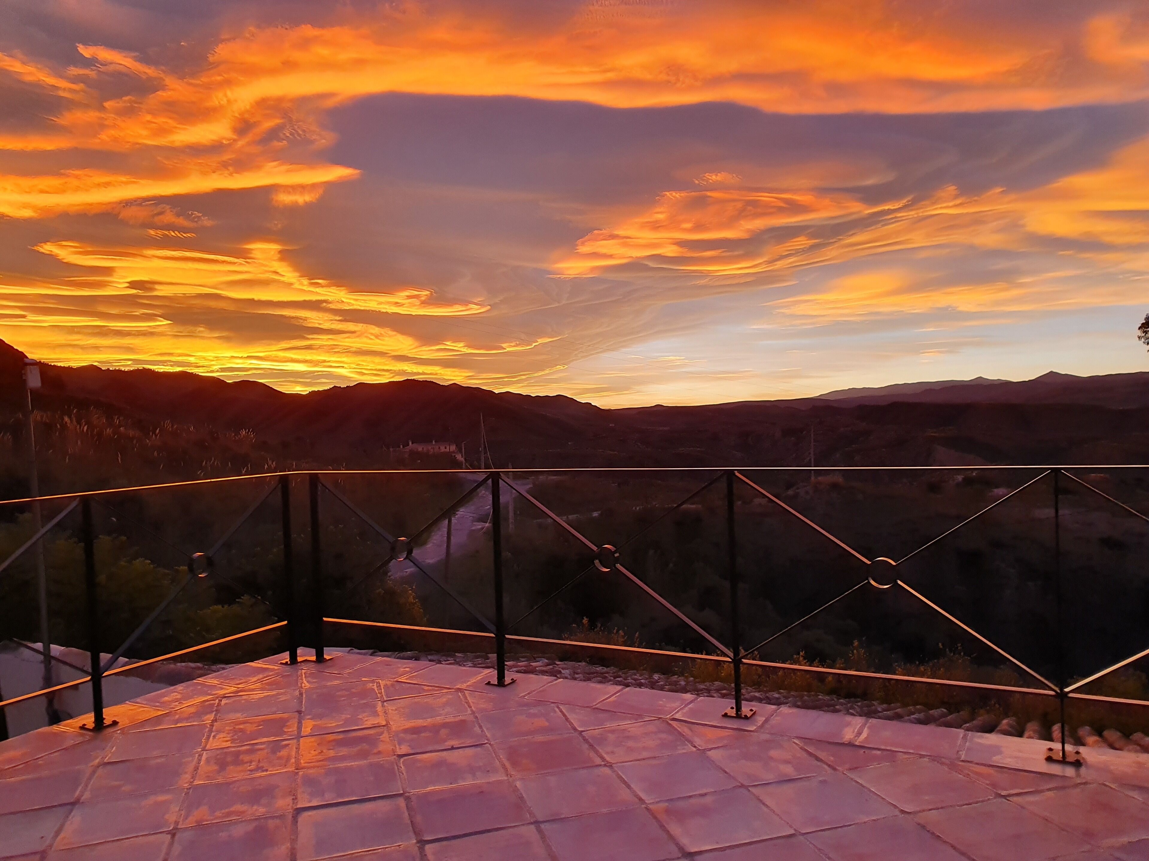 A terrace with a view of a sunset over mountains.