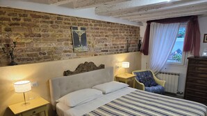 Ein Schlafzimmer mit Backsteinwand, einem Bett mit gestreifter Bettwäsche, einem Sessel, einem Nachttisch und einer Lampe.