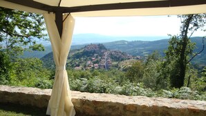Une chambre avec un mur en pierre, un lit recouvert d’une literie à motifs floraux et une vue sur un village et des montagnes.