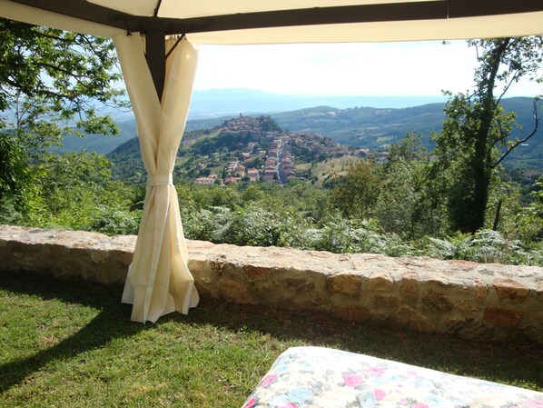 Une chambre avec un mur en pierre, un lit recouvert d’une literie à motifs floraux et une vue sur un village et des montagnes.
