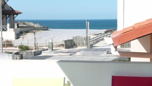A beach view with a wooden walkway leading to the water, a building with a red roof, and a clear blue sky.