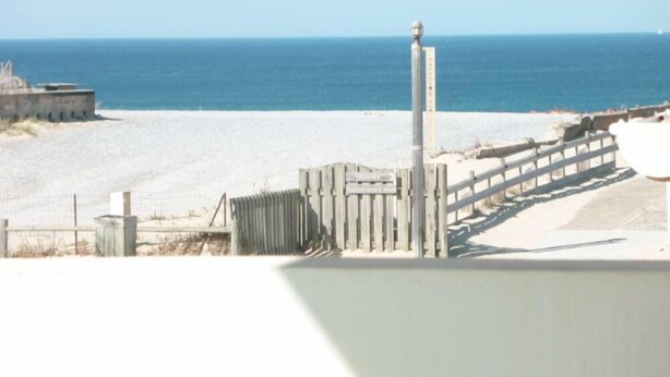 A beach view with a wooden fence, a metal pole, and a concrete structure.