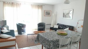 A living room with a sofa, a dining table with chairs, a TV, and a window with curtains.