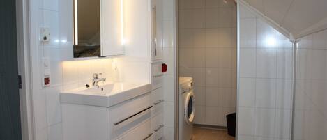 A modern bathroom with a white sink, mirror, and built-in washing machine.