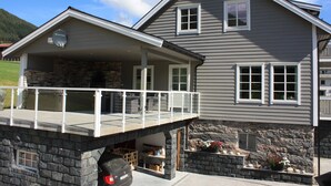 A two-story house with a stone foundation, a covered porch, and a garage. - Newly built, high-quality holiday home close to Viksdalsvatnet — sleeps 9 (Viksdalen)