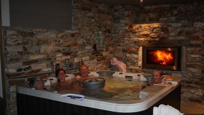 A stone-walled room with a stone fireplace and a hot tub with three people. - Newly built, high-quality holiday home close to Viksdalsvatnet — sleeps 9 (Viksdalen)