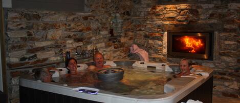 A stone-walled room with a stone fireplace and a hot tub with three people.