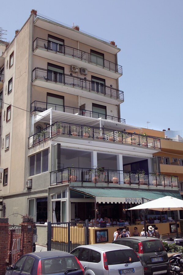 A multi-story building with balconies, a restaurant on the ground floor, and parked cars in front. - Casa d'A..Mare flat seafront beautiful terrace with extraordinary beach view (Giardini Naxos)
