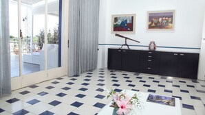 Una stanza con pavimento a scacchi, un divano bianco, un armadietto nero e due quadri appesi al muro.