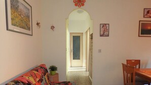 Un pasillo con un sofá, una mesa de comedor y sillas, que conduce a una puerta.