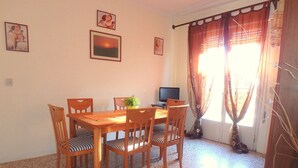 Un comedor con una mesa y sillas de madera, un televisor y una ventana con cortinas.