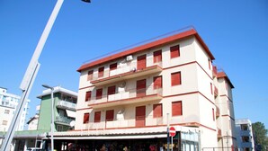Un edificio de varios pisos con fachada roja y blanca, balcones y una tienda en la planta baja.