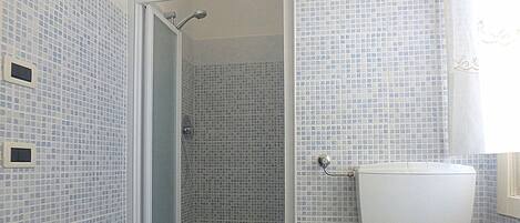 Baño con ducha, paredes de azulejos y retrete.