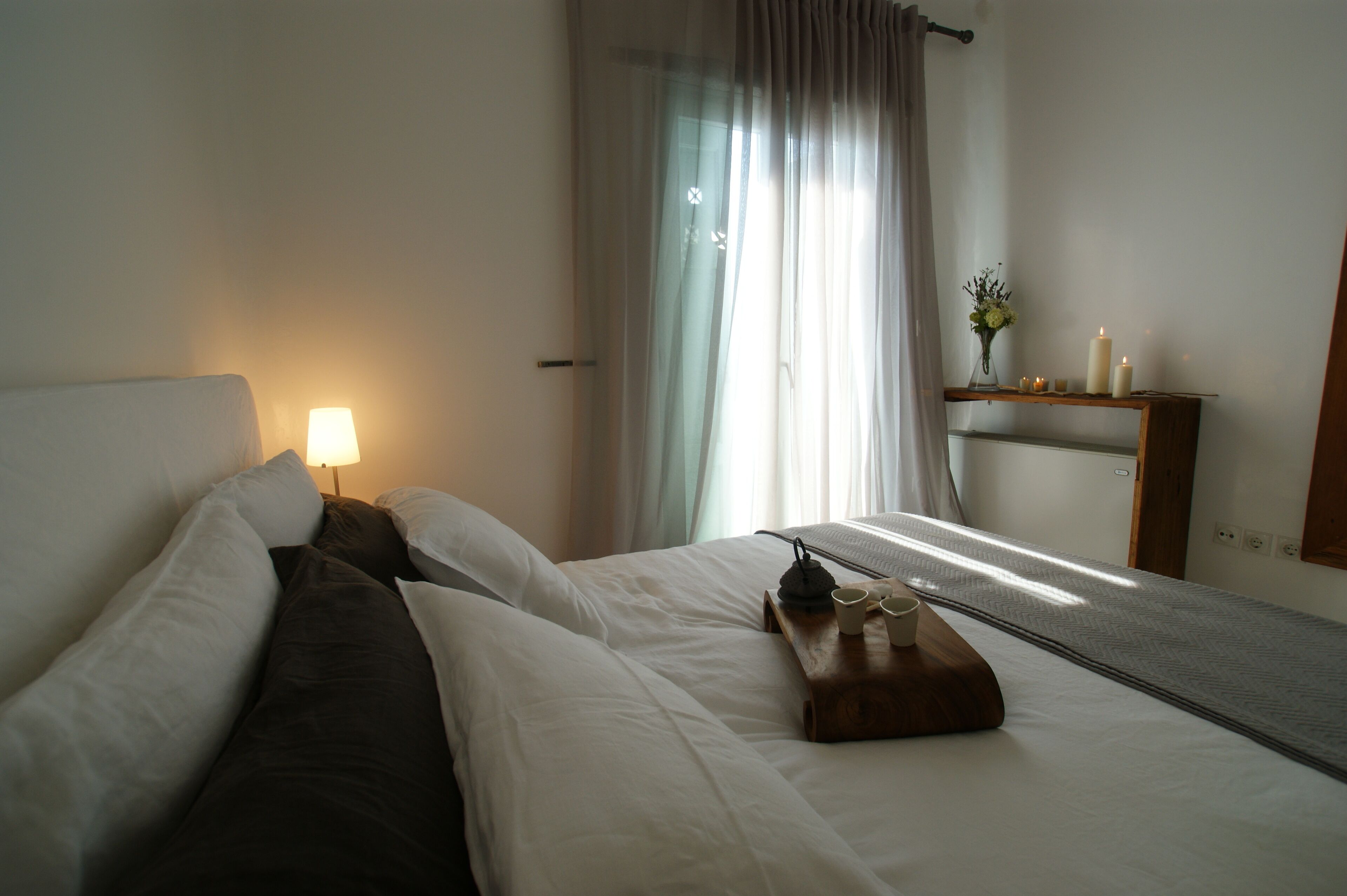 A hotel room with two beds, a bedside table with a lamp, a small table with cups, and a mirror on the wall.