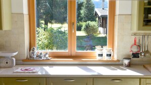 A kitchen with a window view of a house and garden, a scale, a tea set, and jars labeled "ZUCCHERO" and "SALE".